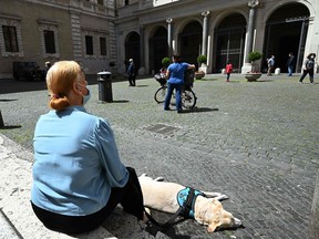 A woman and her dog pause outside Rome's Santa Maria in Trastevere square on May 3, 2020, during the country's lockdown aimed at curbing the spread of the COVID-19 virus.