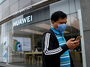A man wearing a face mask uses his mobile phone as he walks past a Huawei store in Beijing on May 16, 2020.