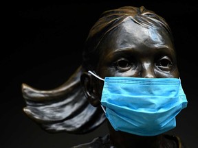 The "Fearless Girl" bronze sculpture, is seen wearing a mask in front of the New York Stock Exchange.