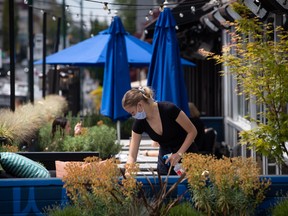 A server wears a face mask while cleaning a table on the patio at an Earls restaurant, in Vancouver, on Tuesday, May 19, 2020.