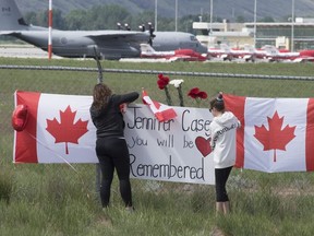 The Canadian Forces Snowbirds jets are seen in the background as women attach a sign to a fence in Kamloops, B.C., Monday, May 18, 2020.
