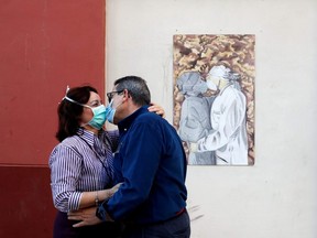 Maria Rosa Iglesias and Alfonso Garcia, both nurses aged 58, wear masks and kiss next to a wall painting in support of healthcare workers in Malaga, Spain on May 18, 2020.