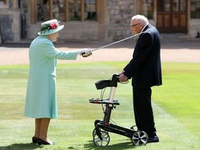 Britain's Queen Elizabeth II uses the sword that belonged to her father, George VI as she confers the Honour of Knighthood on 100-year-old veteran Captain Tom Moore at Windsor Castle in Windsor, west of London on July 17, 2020.