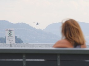 A woman on a bench at Skaha Beach watches a heli-tanker lift off from Skaha Lake en route to the nearby Christie Mountain fire.