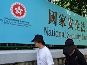 Pedestrians walk past a government public notice for the National Security Law in Hong Kong.