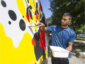 Sarbjot Atwal works on a mural entitled 'Common-unity,' on a fence near the King George Skytrain station in Surrey, Aug. 13, 2020.