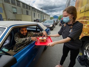Samantha Douglass transfers poutine to Tarun Minhas who drives a '72 Mustang during the PNE Car-B-Que in Vancouver, B.C., June 21, 2020.