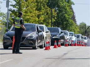 A Vancouver police officer monitors a line of cars waiting to access the COVID-19 testing site near Cambie and West 33rd.