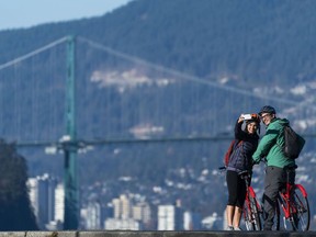 A couple stops for a selfie with the Lions Gate Bridge in the background.