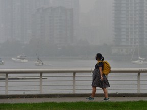 A woman wearing a face mask walks as smoke from wildfires in neighbouring Washington state shrouds False Creek in Vancouver, British Columbia, Canada September 14, 2020.