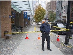 A Vancouver police constanble steers pedestrians away from an area in front of an optometry store at 806 West Hastings Street in Vancouver on Oct. 5, 2020, closed by a fire department hazmat crew after mercury droplets were discovered on the sidewalk in front of the shop.