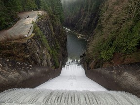 Water flows over the Cleveland Dam as people walk with a dog in Cleveland Park in North Vancouver, B.C., on Christmas Day, Friday Dec. 25, 2015.