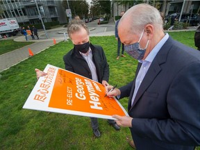 B.C. Premier John Horgan signs NDP candidate George Heyman's re-election sign at Olympic Village in Vancouver on Monday.