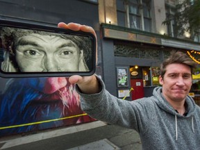 Jameson Trenholm, holding a phone with an image of Chi Pig, with the half-finished mural, in the background, of punk rock legend Chi Pig on the side of the Cambie Hotel in Vancouver on Oct. 28.