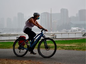 A woman wearing a face mask cycles as smoke from wildfires in neighbouring Washington state shrouds False Creek in Vancouver, Sept. 14, 2020.