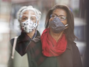 People are reflected in a window as they wear face masks on a street in Montreal, Saturday, Nov. 14, 2020, as the COVID-19 pandemic continues in Canada and around the world.