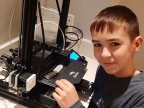 Nickolai Junussov with his 3D printer. The 12-year-old spends his spare time improving the comfort of masks for first responders.