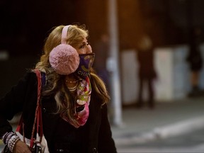 A woman wearing a protective face mask and earmuffs crosses the street during the COVID-19 outbreak, in Beverly Hills, Calif., Nov. 20, 2020.