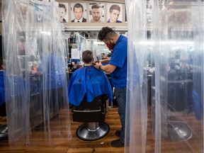 Fady Danial cuts Robert Bruce's hair at a barbershop that has erected plastic shower curtains as a measure to help curb the spread of COVID-19, in Burnaby. British Columbia announced new public health measures for the Vancouver Coastal Health and Fraser Health regions on Saturday — including an order for people not to have social interactions outside their immediate household and a ban on indoor group physical activities for two weeks.