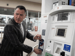 Ontario Energy Minister Greg Rickford applies an anti-carbon tax sticker to a gas pump, April 8, 2019.