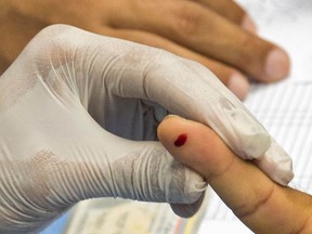 A doctor holds the finger of a man with a drop of blood during a COVID-19 quick test in a file photo.