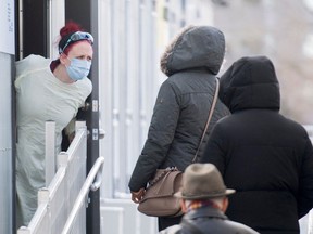 healthcare worker talks with people as they wait to be tested for COVID-19 at a clinic in Montreal, Sunday, Dec. 27, 2020, as the COVID-19 pandemic continues in Canada and around the world.
