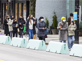 People wearing masks line up to enter a store in downtown Vancouver.