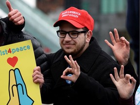 Angelo Isidorou, right, and a small group of University of B.C. students pose for a photo wearing 'Make America Great Again' hats at an Anti-Trump protest at Jack Poole Plaza on Feb. 28, 2017.
