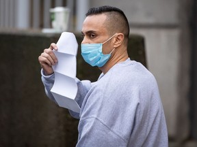 Mohammad Movassaghi tries to hide his face with a copy of his release order as he leaves Vancouver Police Department jail in Vancouver on Sunday, Jan. 31, 2021. Police arrested a man who allegedly operated a makeshift nightclub at his Vancouver penthouse and issued fines against him and his suspected guests totalling more than $17,000.