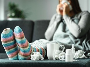 Sick woman with flu, cold, fever and cough sitting on couch at home.