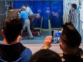 Mourners wearing facemasks are reflected in the glass as they livestream a cremation.