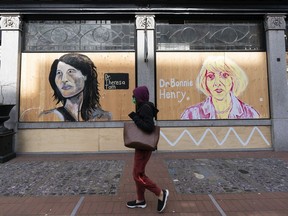 A woman walks past murals painted of Dr. Theresa Tam and Dr. Bonnie Henry on the side of a building in Gastown in Vancouver, BC. Both Henry and Tam have said that the spread of misinformation about the pandemic and vaccines continues to be a major challenge.
