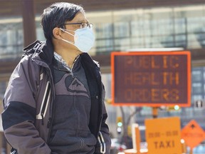 A man stands next to a COVID-19 restrictions sign in Calgary on Tuesday, April 6, 2021. COVID-19 case numbers have continued to rise.