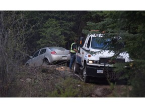 A car is hauled from the bush Monday night off the Arawana Forest Service Road near Penticton. Police were called to a report of "suspicious circumstances" on the road Monday around the same time two dead bodies were found on nearby Naramata Creek forest service road.