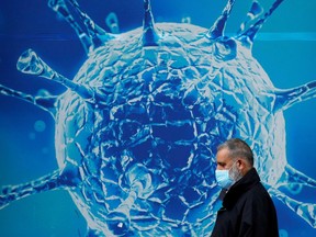 A man wearing a protective face mask walks past an illustration of a COVID virus.