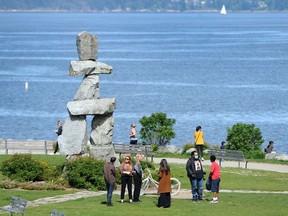 Socially-distanced sun seekerse enjoy a warm day near the Inukshuk sculpture along English Bay in Vancouver.