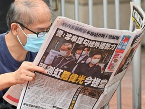 This file photo taken on June 19, 2021 shows a supporter reading a copy of the Apple Daily newspaper outside a court in Hong Kong, after the two Apple employees were charged with collusion over their newspaper's coverage after authorities deployed a sweeping security law.