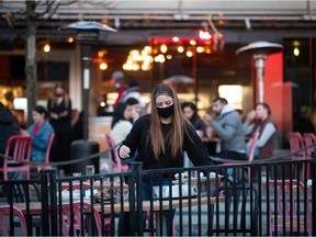 A server clears a table on a patio at a restaurant, in Vancouver, on Friday, April 2, 2021.
