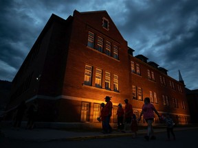 People are silhouetted as they walk past the former Kamloops Indian Residential School after gathering to honour the 215 children whose remains have been discovered buried near the facility, in Kamloops on Monday, May 31, 2021.