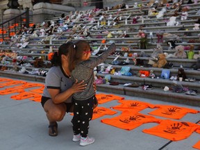 Emmy Morris who attended Indian day school and her mother who went to a residential school joins her daughter Sharon Morris-Jones, 4, from the Tsartlip First Nation as they look at the Orange shirts, shoes, flowers and messages on display on the steps outside the legislature in Victoria, B.C., on Tuesday, June 8, 2021 following a ceremony hosted by the Songhees and Esquimalt First Nations in honour of the 215 residential schoolchildren whose remains have been discovered buried near the facility in Kamloops, B.C.