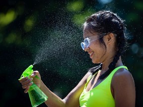 Leanne Opuyes uses a spray bottle to mist her face while cooling off in the frigid Lynn Creek water in North Vancouver on Monday. Environment Canada said the torrid heat wave will start easing on Wednesday.