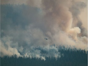 A helicopter with a water bucket flies past the Tremont Creek wildfire burning on the mountains above Ashcroft, B.C., on Friday, July 16, 2021.