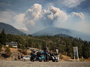 Motorcyclists stopped at a gas station watch as a pyrocumulus cloud, also known as a fire cloud, produced by the Lytton Creek wildfire rises into the sky from the fire burning in the mountains above Lytton, B.C., on Sunday, August 15, 2021.