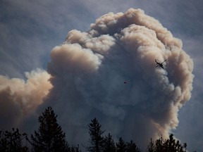 A helicopter carrying a water bucket flies past a pyrocumulus cloud, also known as a fire cloud, produced by the Lytton Creek wildfire burning in the mountains above Lytton on Sunday, August 15, 2021.