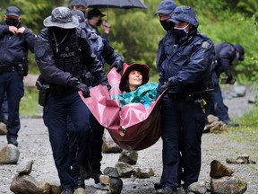 RCMP officers carry a woman they arrested at the Waterfall camp blockade against old growth timber logging in the Fairy Creek area of Vancouver Island on May 24, 2021.