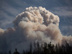 A helicopter carrying a water bucket flies past a pyrocumulus cloud, also known as a fire cloud, produced by the Lytton Creek wildfire burning in the mountains above Lytton.
