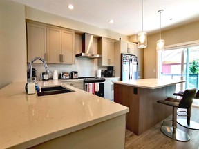 The kitchen in this four-bedroom Langley townhome has quartz countertops, a double undermount sink, Shaker-style cabinets and a centre island with overhead pendant lighting.