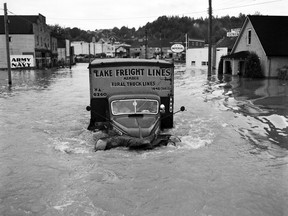 1948 Fraser River Flood - Mission - Two men maneuver a truck, labeled "Lake Freight Lines Member: Rural Truck Lines" down a street; Army & Navy sign seen in the background. 1948.