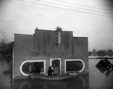 1948 Fraser River Flood - Mission - An unidentified male in a canoe opens the screen door to the Player's Please[?] cafe and pharmacy. 1948. Vancouver Sun.