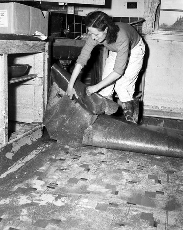 1948 Fraser River Flood - Mission - A woman wearing galoshes removes water-damaged linoleum kitchen flooring. 1948. Vancouver Sun.